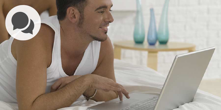 Gay man in white singlet using laptop to video chat.
